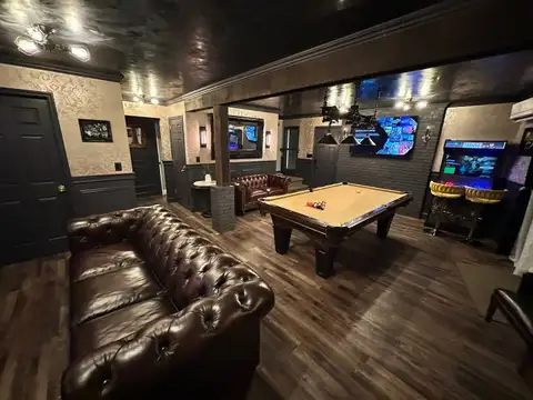 Leather Chesterfield sofa, pool table, smart TV and retro arcade machine in the speakeasy game room