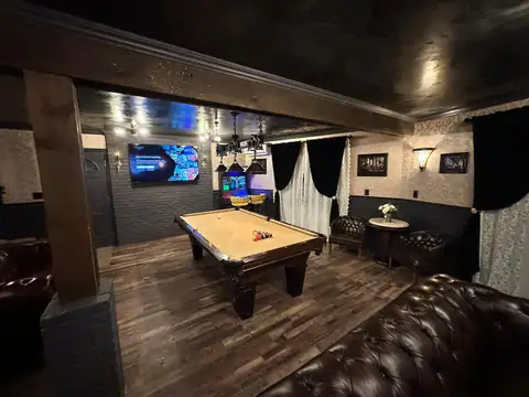 Pool table racked for a game beneath a wrought-iron chandelier, with velvet and lace curtains and cafe table
